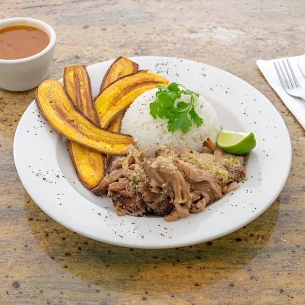 Amore Sabores' catering dish with shredded pork, white rice, fried plantains, lime, and a side of sauce.