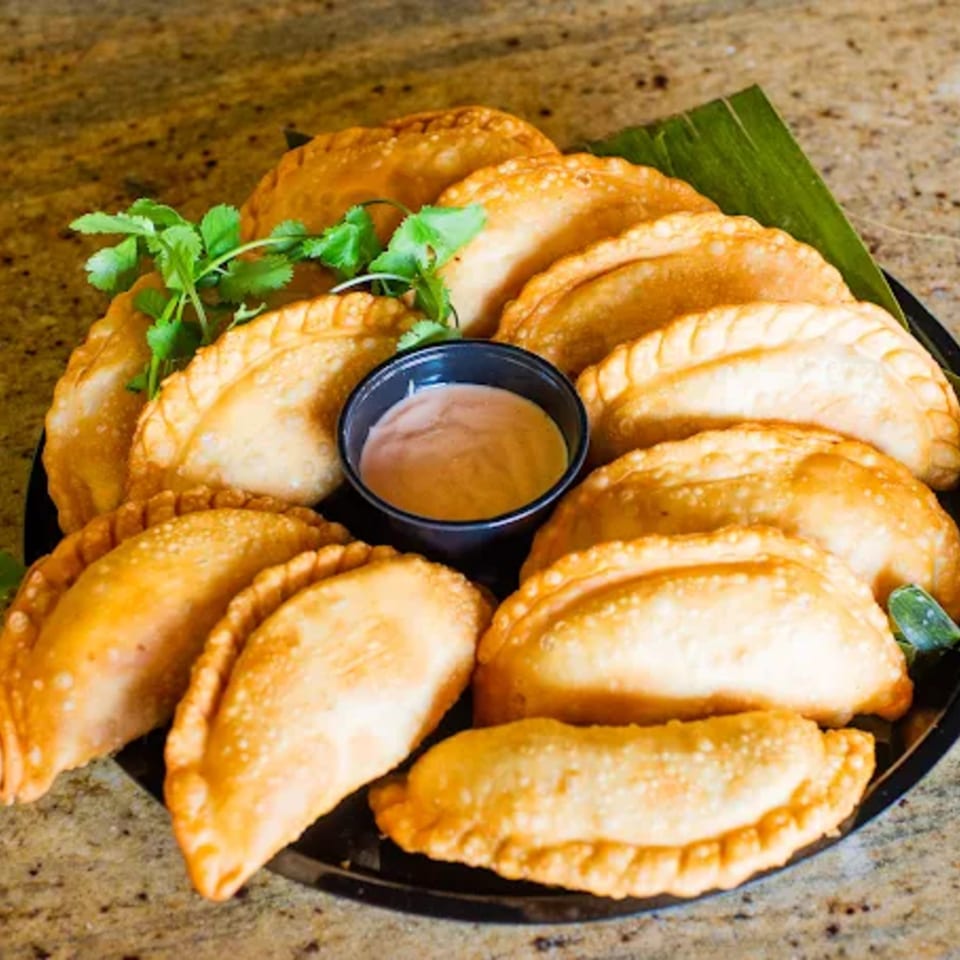 A black platter filled with golden-brown Amore Sabores empanadas, garnished with cilantro and a dipping sauce.