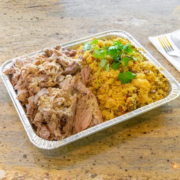 A catering tray of Amore Sabores' shredded pork and yellow rice with cilantro on a granite counter.