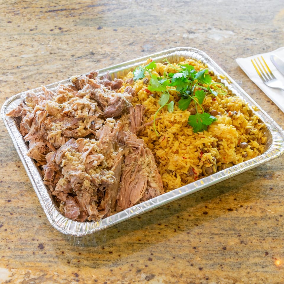 A catering tray filled with shredded pork and yellow rice with beans, garnished with cilantro.