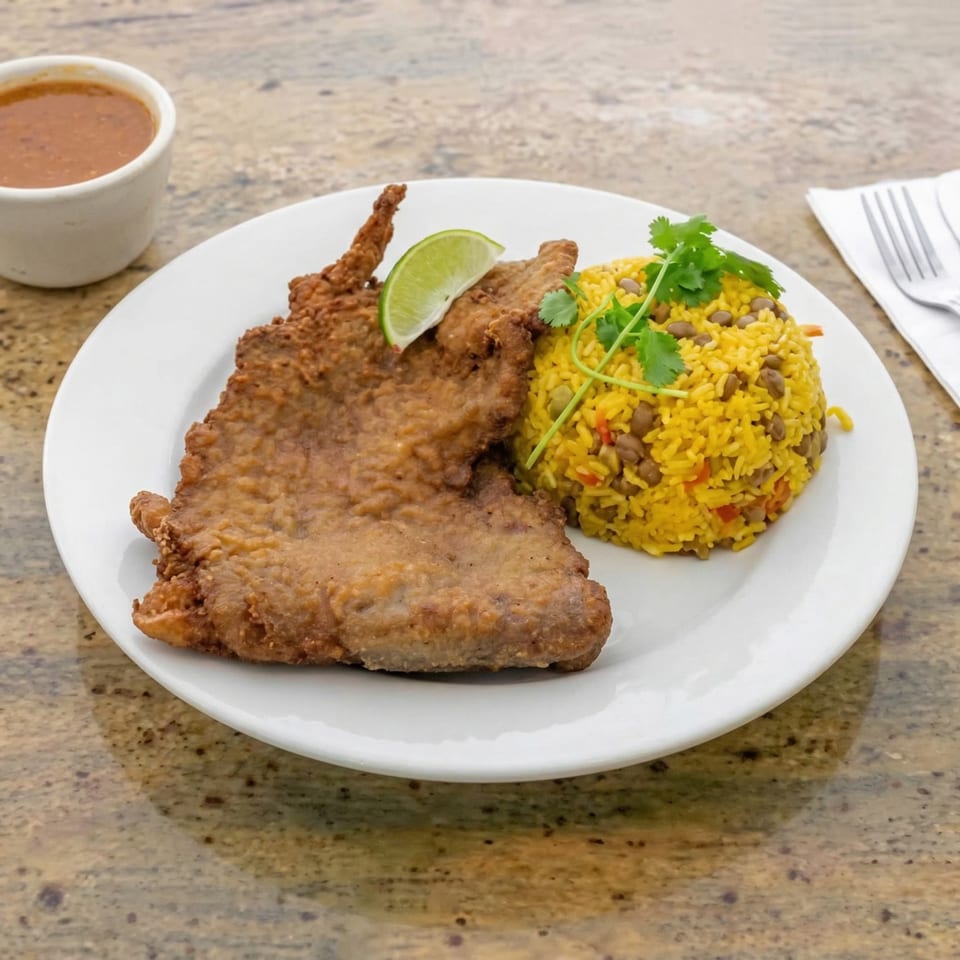 Amore Sabores catering: Fried fish with yellow rice, beans, cilantro, and a lime wedge, with a side of sauce.